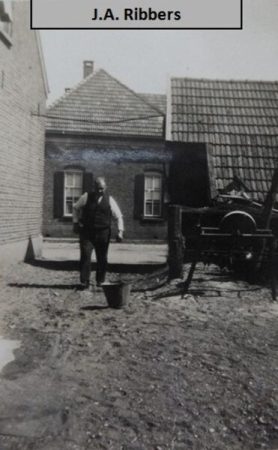 J.A. Ribbers lopend op het onverharde huispeceel. Rechts de schuur waaruit meel/veevoer werd verkocht. Op de achtergrond de boerderij van Hassink-Schreur. Aan de voorkant van de schuur bevond zich een bordes, die er tijdens de bevrijding (1945) door de Tommies is afgereden. De schuur was zo zwaar beschadigd, dat men heeft besloten om deze af te breken. J.A. Ribbers behalve boer, kruidenier, ook machinist bij de zuivelfabriek.